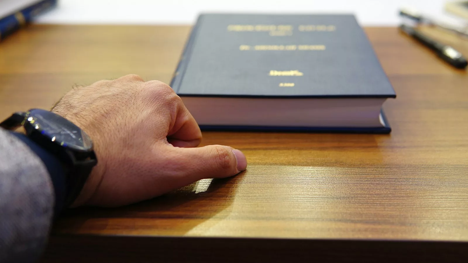Person holding black covered book on brown wooden table